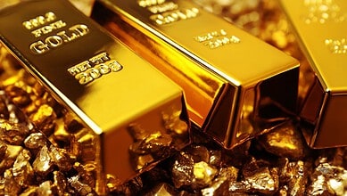 Three gold bars on a bed of gold nuggets, shiny and reflective.