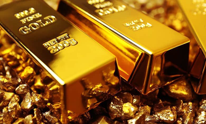 Three gold bars on a bed of gold nuggets, shiny and reflective.
