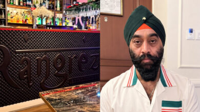 A man with a turban and beard in a white shirt in a restaurant setting, with a bar in the background.