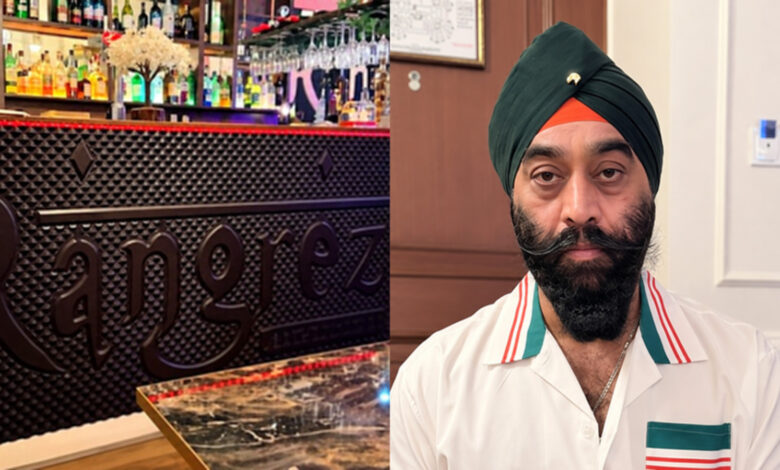 A man with a turban and beard in a white shirt in a restaurant setting, with a bar in the background.