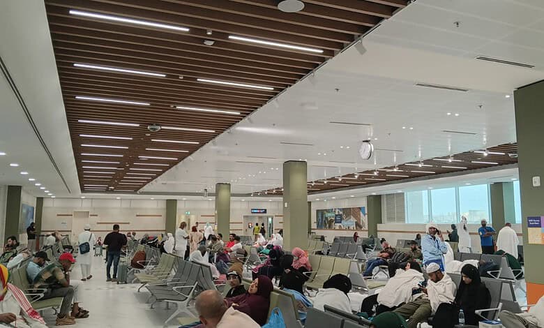 Passengers seated and waiting at Jeddah airport terminal with luggage and staff in background.