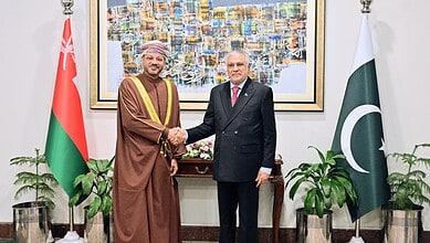 Pakistani and Omani officials shake hands during diplomatic meeting with flags in background.