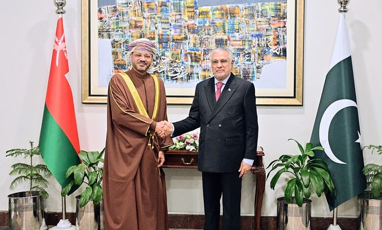 Pakistani and Omani officials shake hands during diplomatic meeting with flags in background.