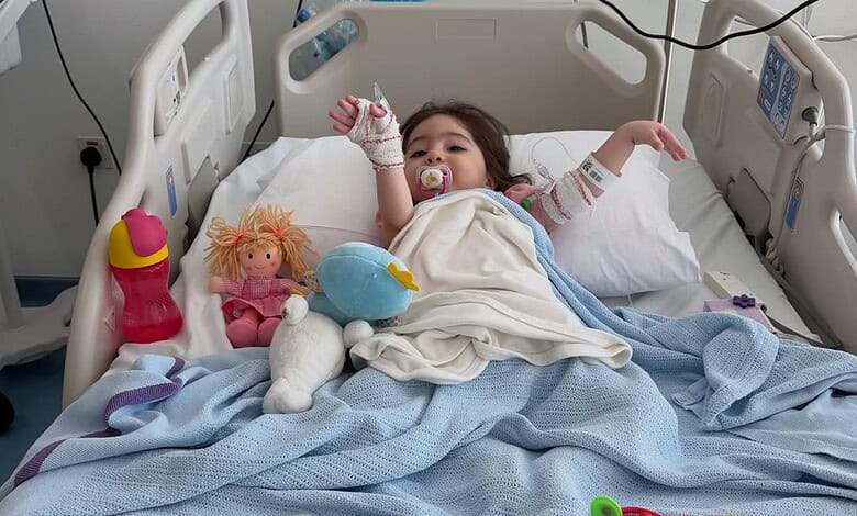 Young girl lying in hospital bed with toys, connected to medical equipment, recovering from treatment.