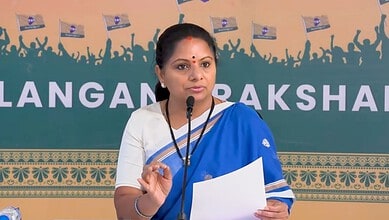 Kavitha speaking at a press conference with a blue and white saree and a microphone.