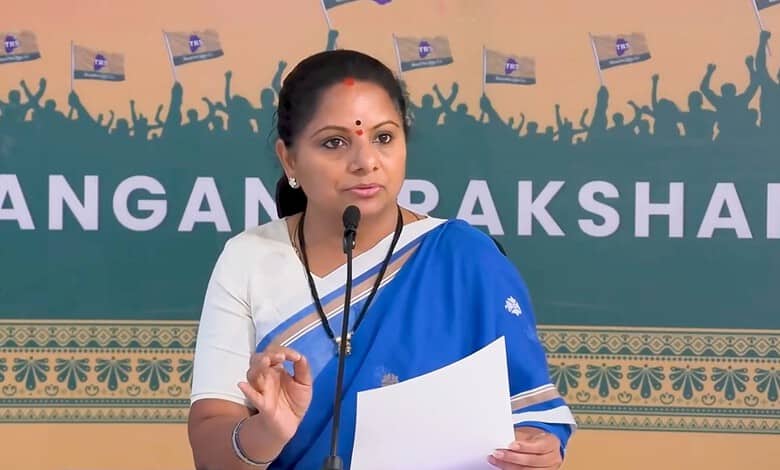 Kavitha speaking at a press conference with a blue and white saree and a microphone.