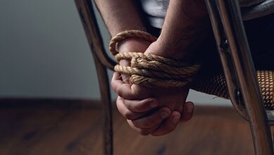 Person handcuffed with rope, sitting on a chair, indicating kidnapping or restraint.