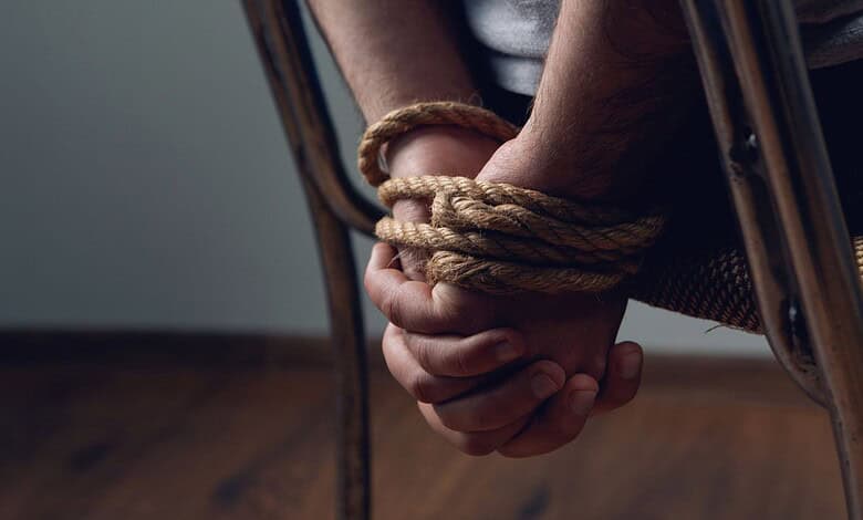 Person handcuffed with rope, sitting on a chair, indicating kidnapping or restraint.