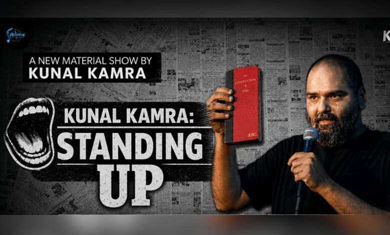 Kunal Kamra holding a red book and microphone during his stand-up show.