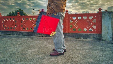 Person holding a red and blue shopping bag on a bridge with a decorative red railing.