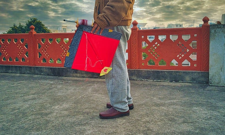Person holding a red and blue shopping bag on a bridge with a decorative red railing.