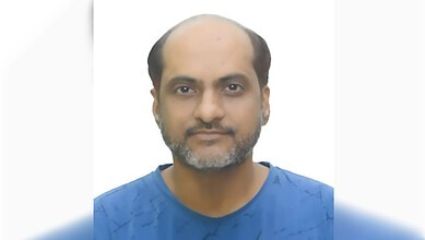 Portrait of a man with a beard and receding hairline wearing a blue shirt.