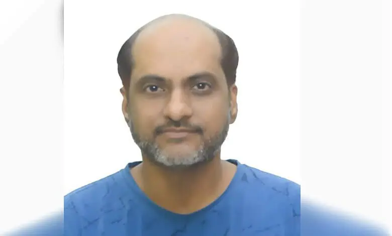 Portrait of a man with a beard and receding hairline wearing a blue shirt.