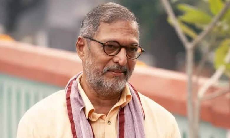 Nana Patekar smiling outdoors with glasses and a beard, wearing a beige shirt and scarf.