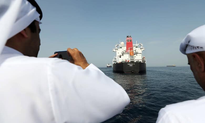 Oil tanker anchored in the Arabian Gulf as men photograph the vessel.