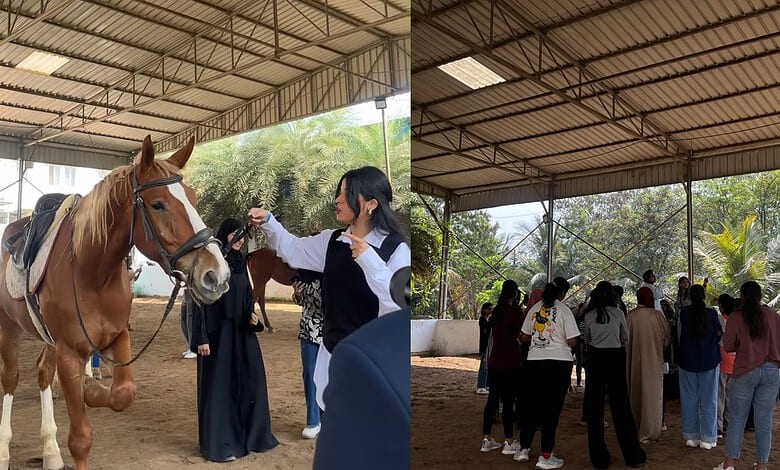 Group of people interacting with horses in an indoor equestrian facility.