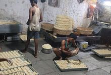 Man preparing traditional Indian snack in a street food setting with large trays of dough.