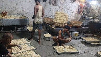 Man preparing traditional Indian snack in a street food setting with large trays of dough.