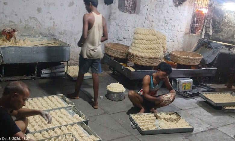 Man preparing traditional Indian snack in a street food setting with large trays of dough.