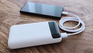 White powerbank connected to smartphone with charging cable on wooden table.