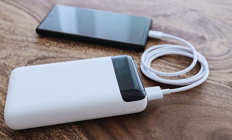 White powerbank connected to smartphone with charging cable on wooden table.