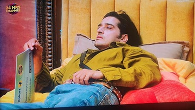 Qazi Touqeer relaxing on a bed with a book in a yellow and orange room.