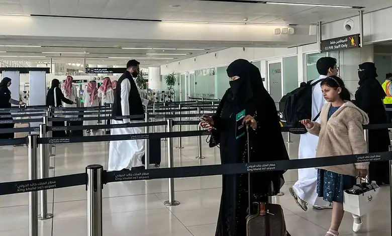 People waiting in line at an airport check-in area with social distancing measures in place.