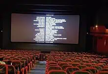Empty theatre hall with red seats and a large screen displaying credits.
