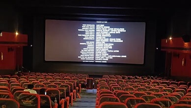 Empty theatre hall with red seats and a large screen displaying credits.