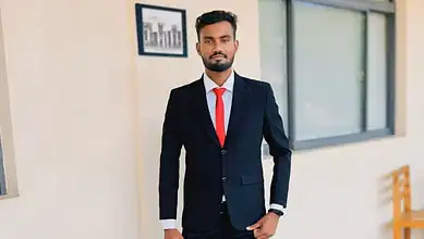 Man in a dark suit with red tie standing in office corridor.