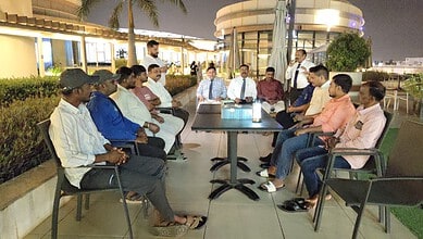 Group of Telugu workers and Oman company representatives in discussion on rooftop terrace.