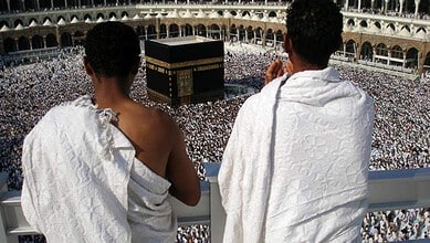 Two pilgrims in white ihram clothing praying at the Masjid al-Haram in Mecca during Hajj.