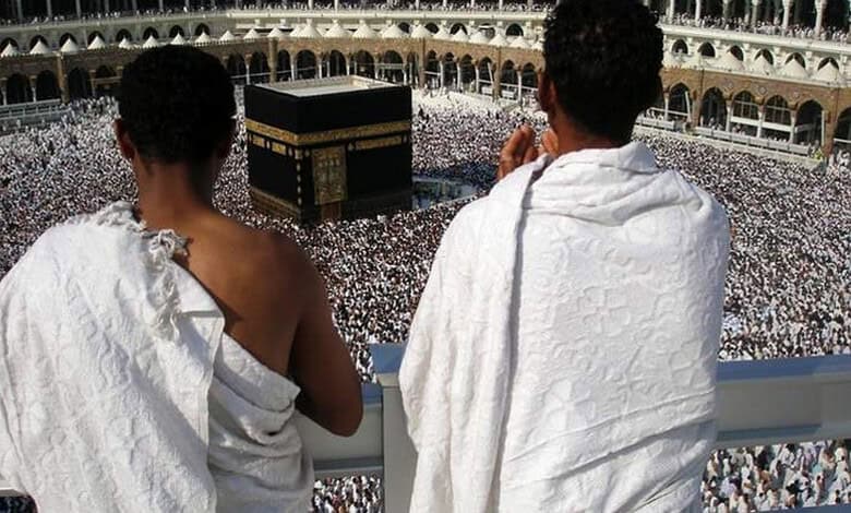 Two pilgrims in white ihram clothing praying at the Masjid al-Haram in Mecca during Hajj.